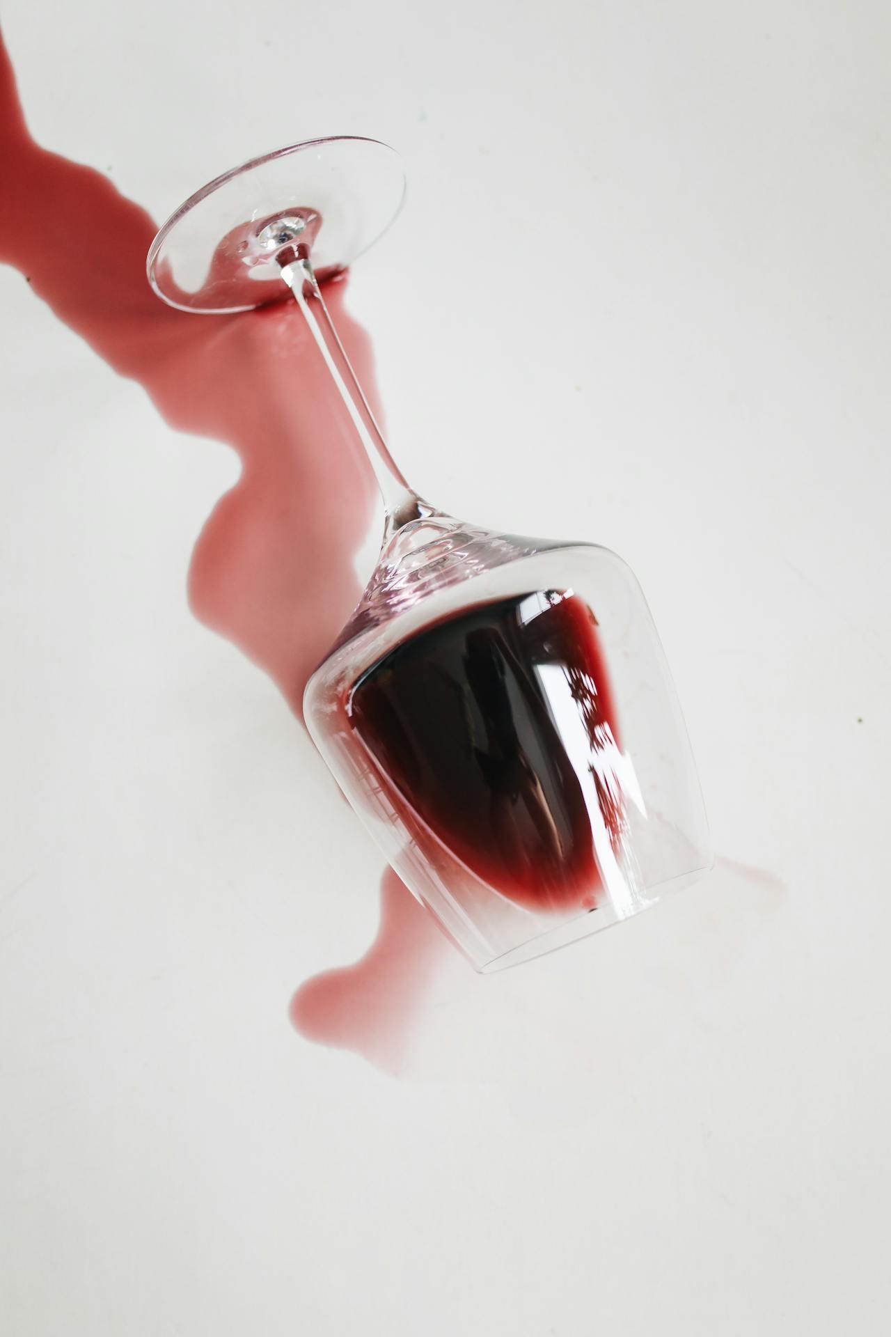 Omgevallen rood wijnglas met uitlopende wijnvlek op witte ondergrond